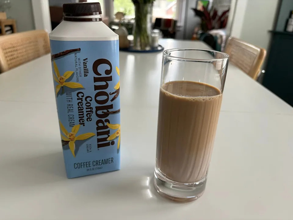 Chobani vanilla coffee creamer next to light-colored glass of coffee