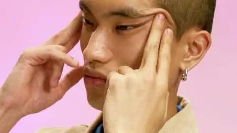Swatch-Nahaufnahme eines jungen asiatischen Mannes, der die Augen der Augen mit beiden Händen hochzieht.