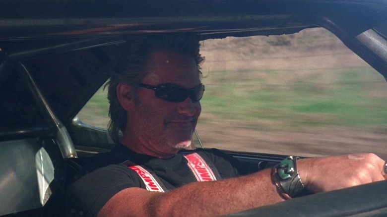 Kurt Russell als Stuntman Mike, die Sonnenbrille trägt, fährt und im Todesbeweis lächelt