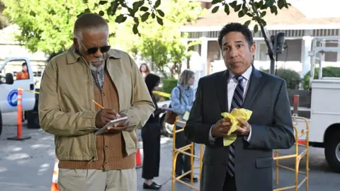Peacock Oscar Nuñez (rechts) als sein Charakter Oscar Martinez im Papier mit einem schwarzen Anzug