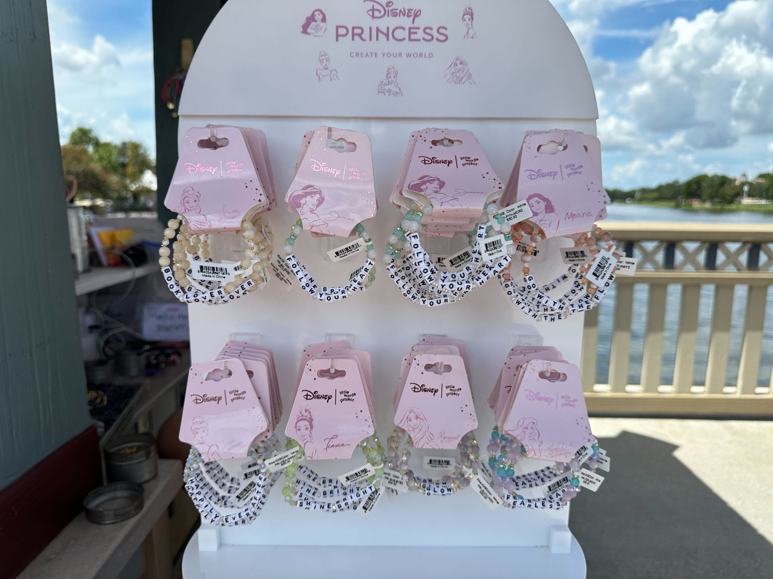 Anzeige von Disney Princess Perlen -Armbändern auf einem weißen Ständer im Freien in der Nähe eines Zauns und Wassers.