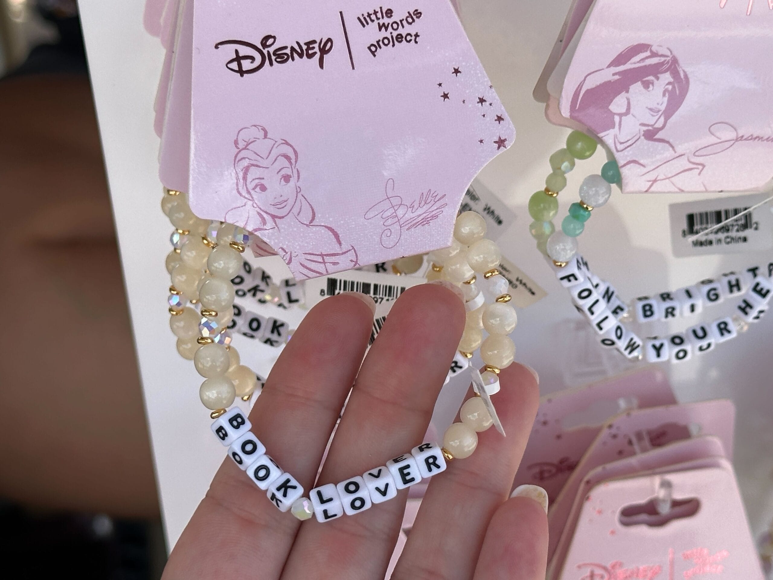 Hand hält ein Perlenarmband, das zaubert "Buchliebhaber," Ausgestellt unter dem Schmuck mit Prinzessinmotiven.