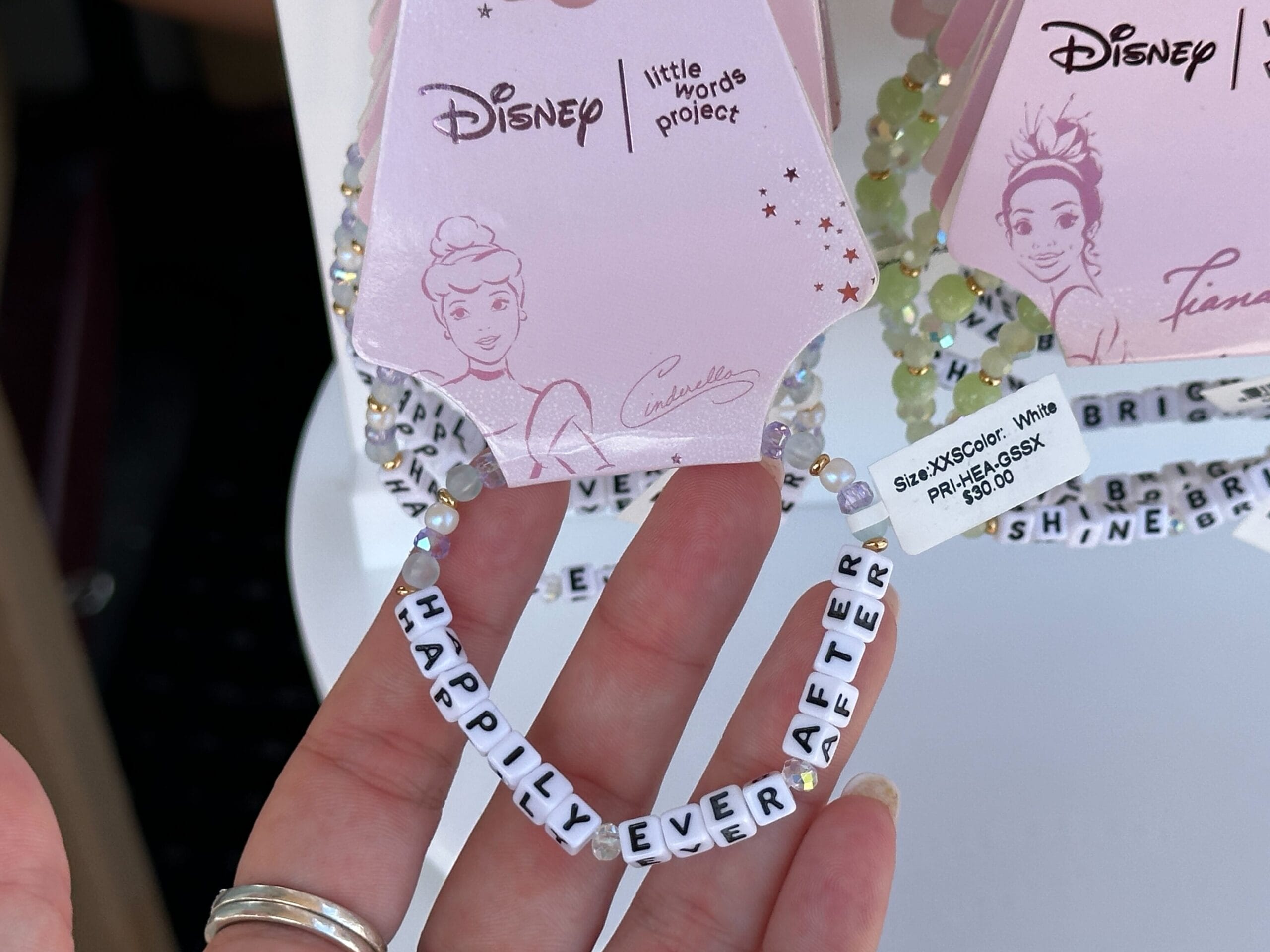 Hand hält ein Perlenarmband mit weißen Buchstabenperlen Rechtschreibung "Glücklich immer danach" und Disney Princess Tag beigefügt.