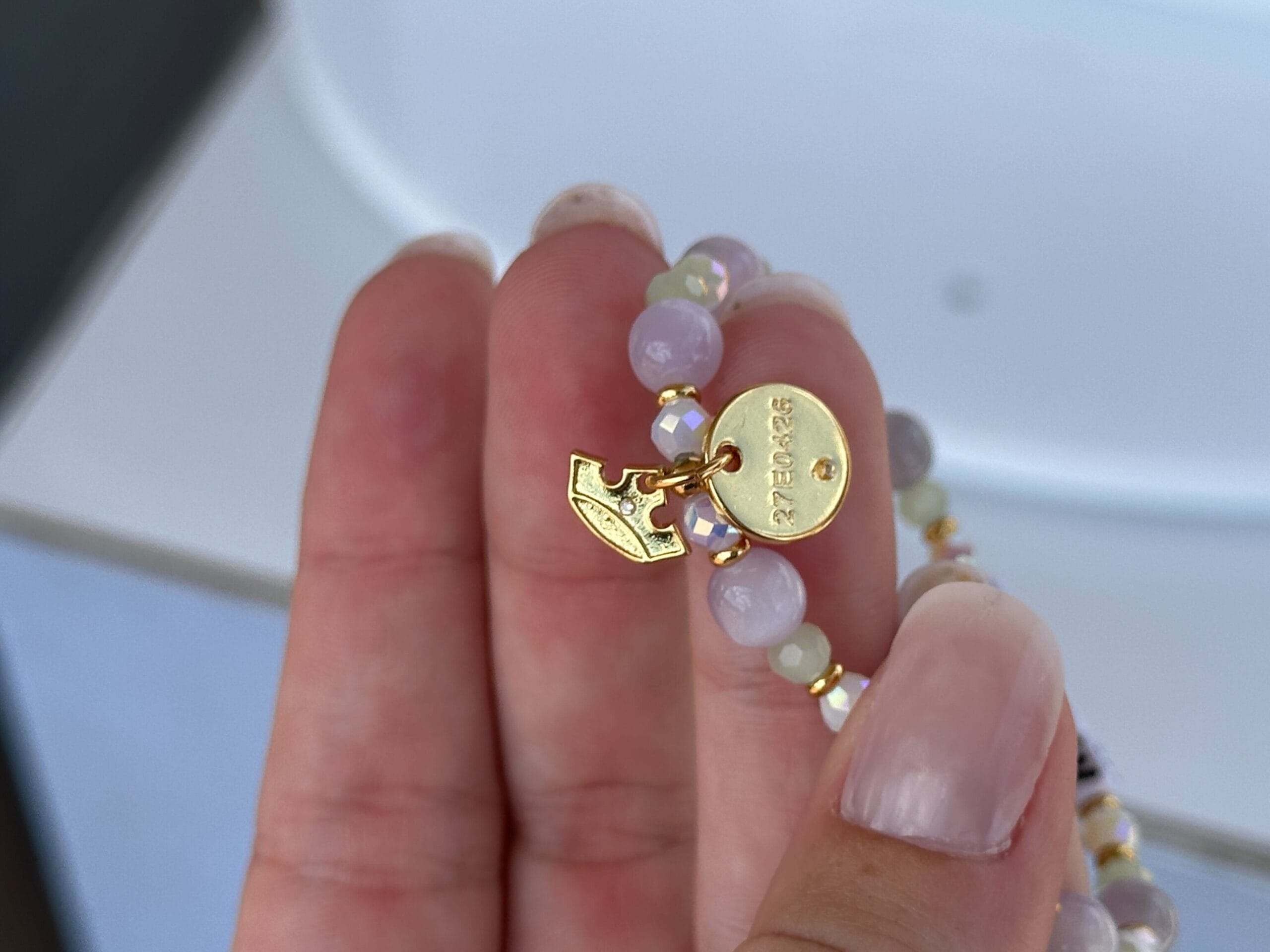 Eine Hand hält ein Perlenarmband mit einem goldenen ovalen Tag eingraviert "ERRATEN" und ein goldener Pfeil.