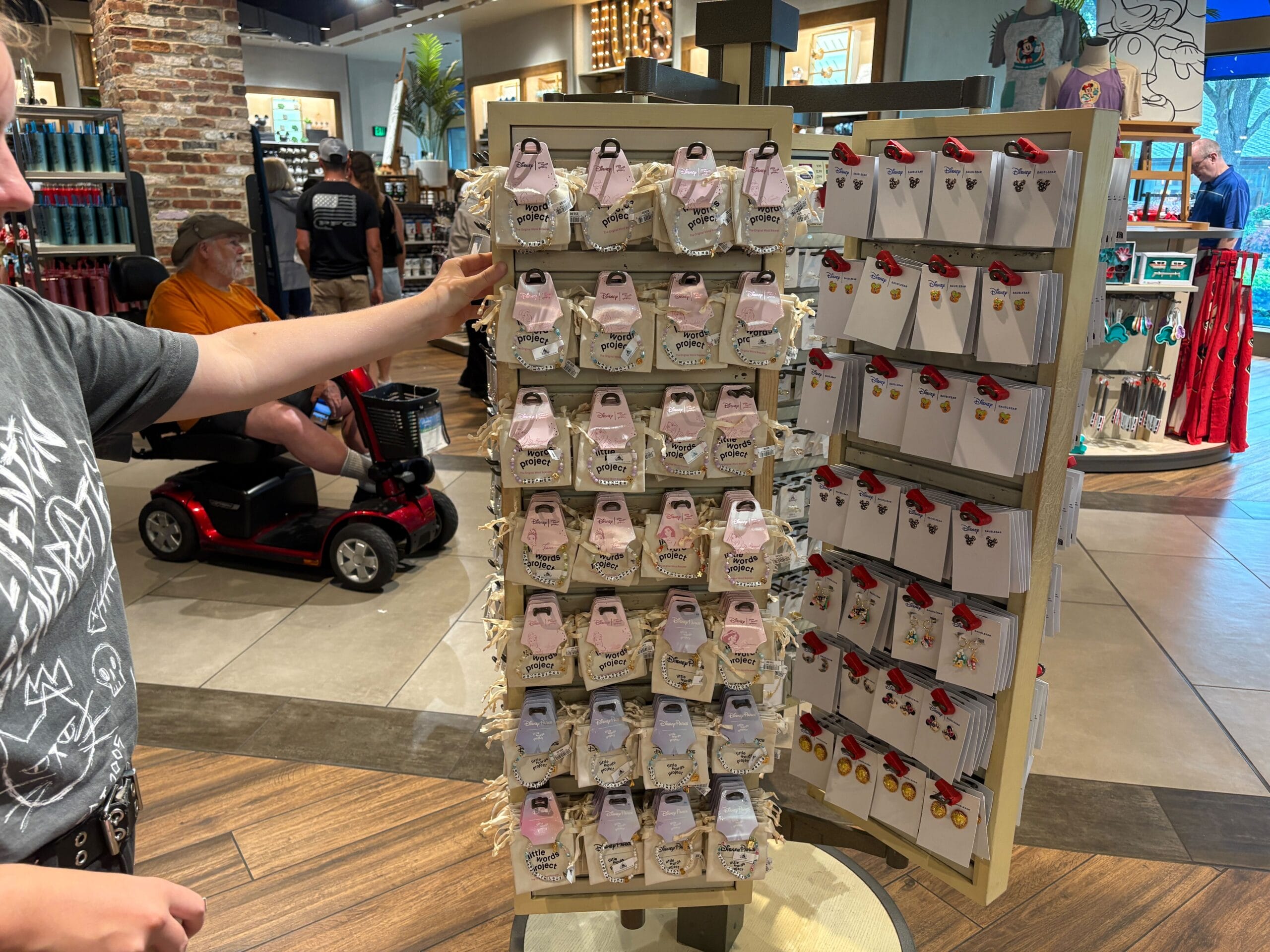 Eine Person betrachtet Souvenirs auf einem rotierenden Displayständer in einem Geschäft, wobei Stifte und Schlüsselanhänger ordentlich angeordnet sind.