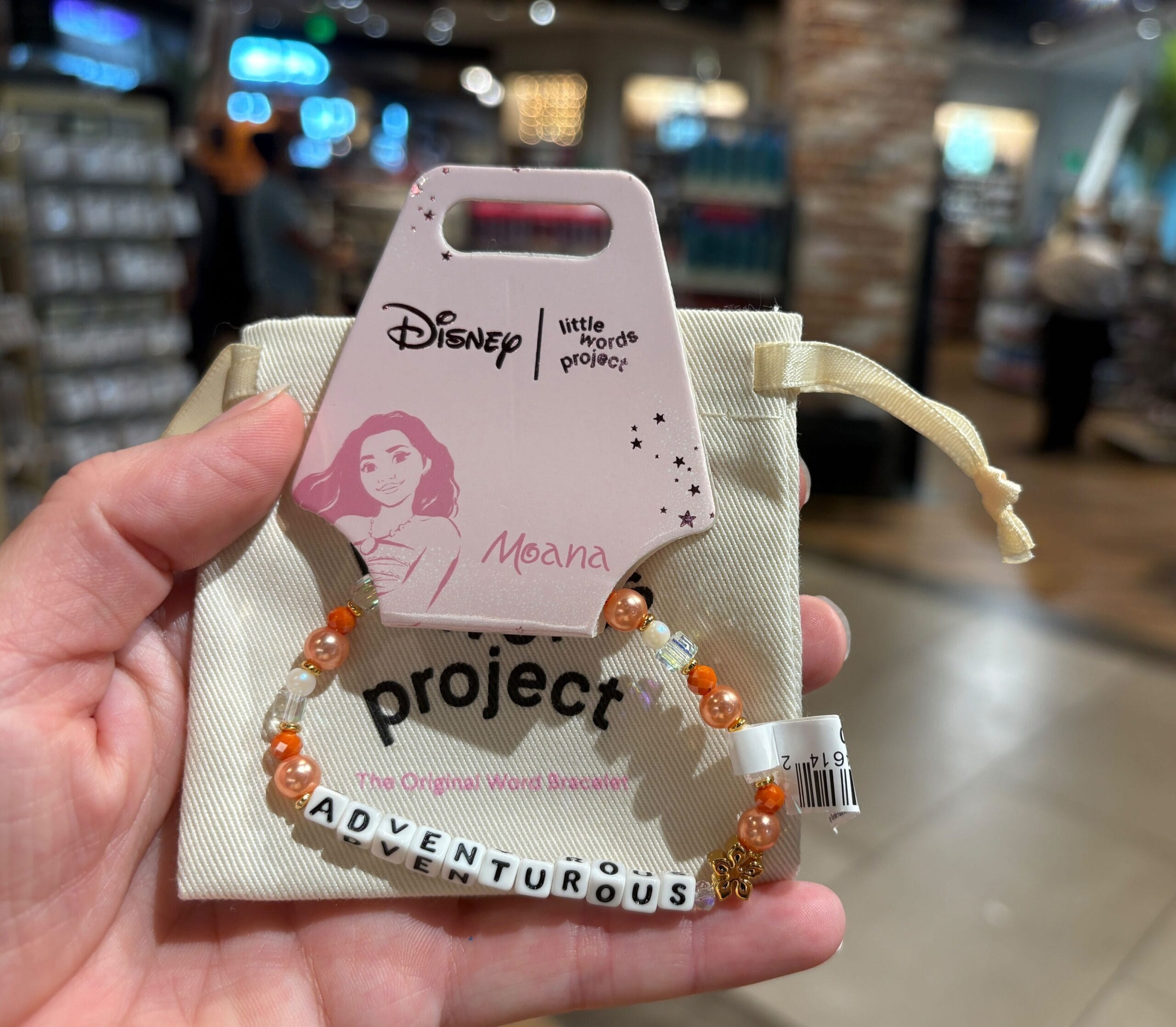 Eine Hand hält eine Schreibweise mit Perlen-Perlen-Brakelet mit Moana "Abenteuerlich" in einem Geschäft.