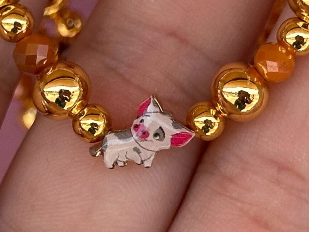 Eine Hand mit einem Perlenarmband mit Gold- und Orangenperlen mit einem Schweinzauber in der Mitte.