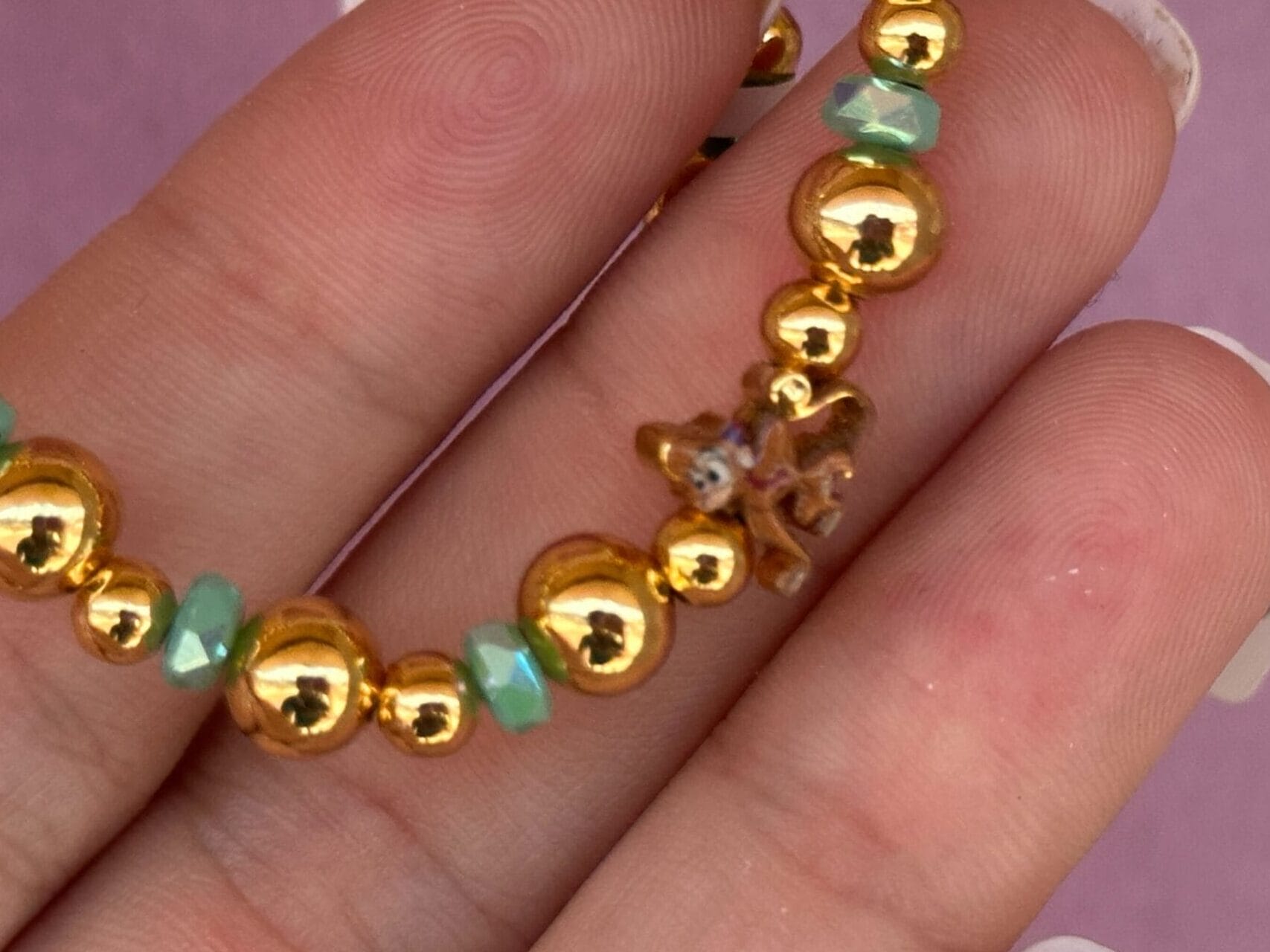 Gold und grünes Perlenarmband mit einem kleinen Seesterne zwischen den Fingern mit gepflegten Nägeln.